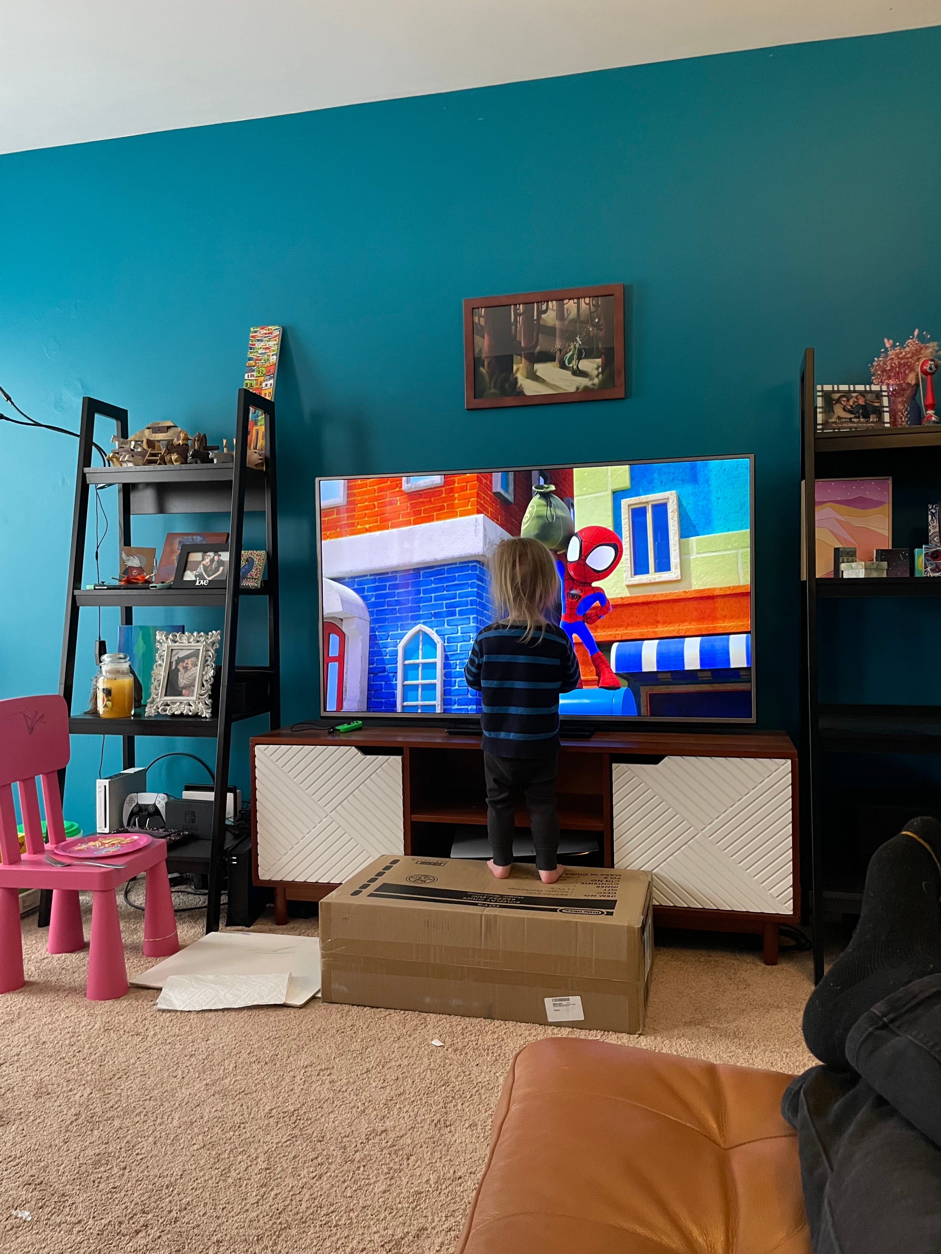 Messy living room, blonde 2 year old standing directly in front of 54 inch television