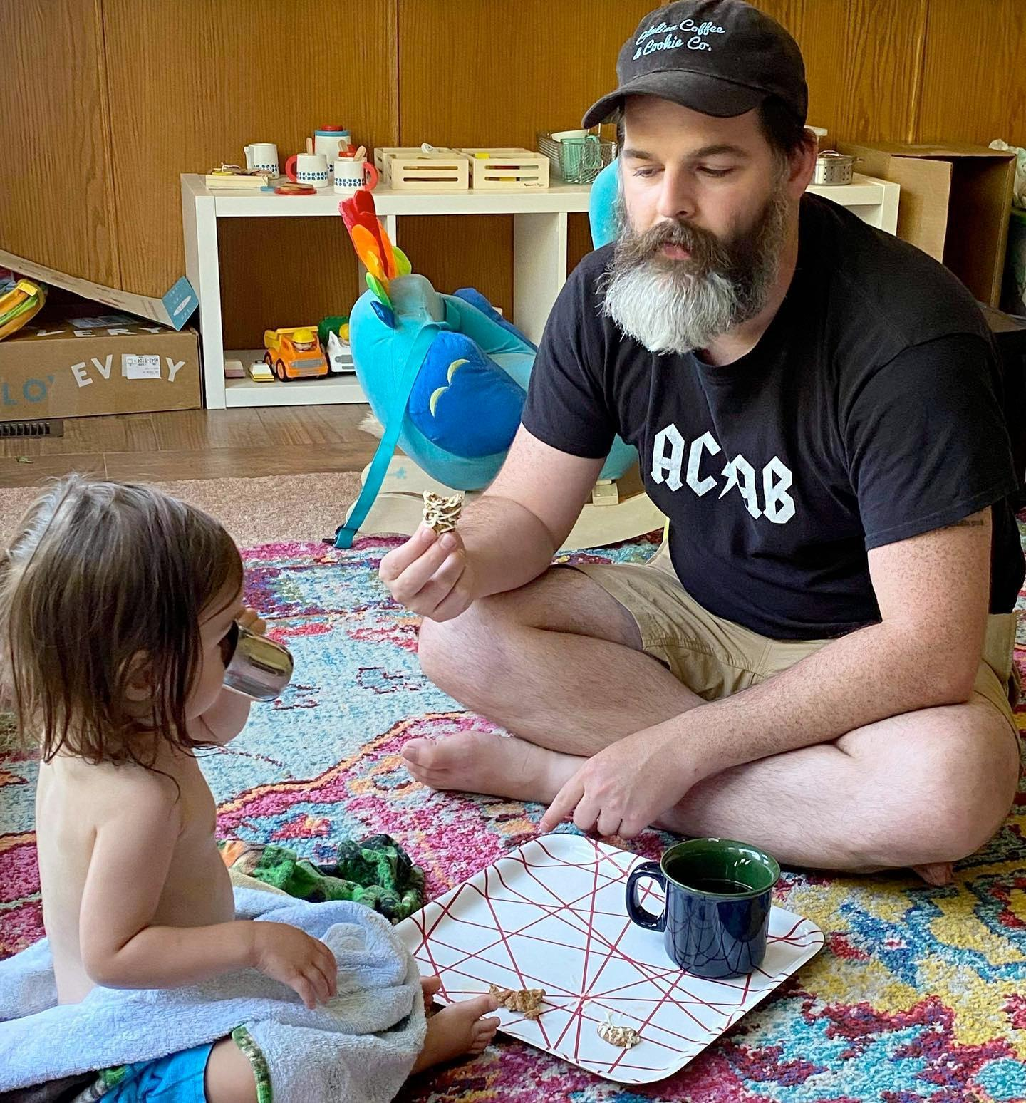 me and my 1.5 year old daughter having a tea party. we're on the oriental rug in our playroom, she's only wearing a towel, i'm wearing my ACAB t-shirt.